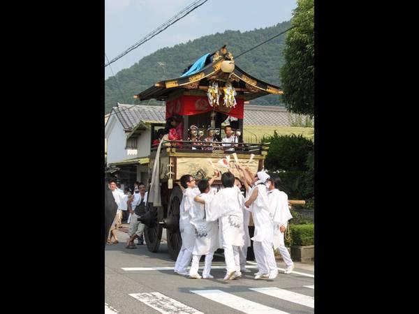 白い衣装を着た男性が神輿を担いでいて、神輿の中に子供が座っている写真