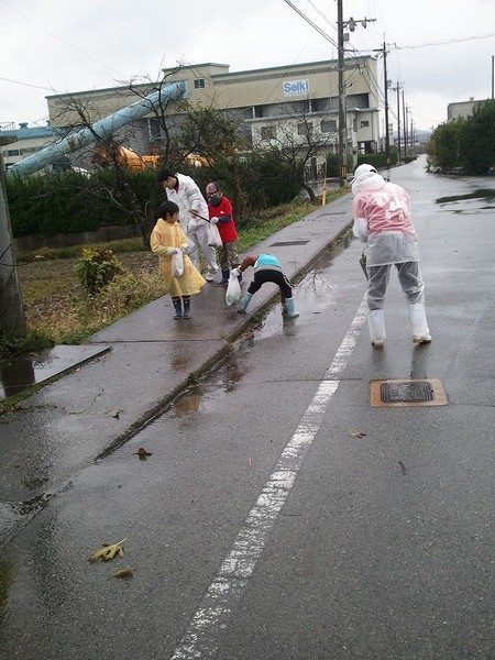 参加者の親子がカッパを着て道路のごみ拾いをしている写真