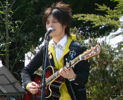ギターを弾きながらスタンドマイクの前で歌っている石田 裕之さんの写真