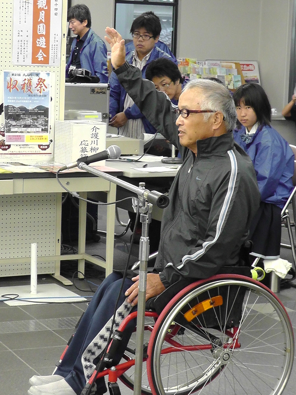 赤い車椅子の男性がマイクの前で、選手宣誓をしている様子の写真