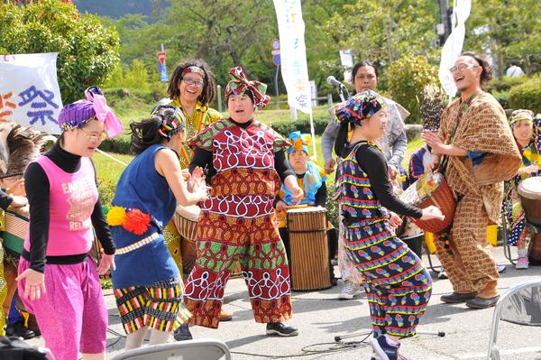 外のステージで民族衣装を着たグループが打楽器の演奏に合わせて踊っている写真