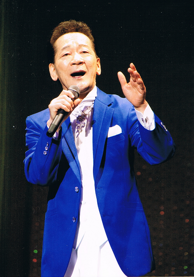 青いジャケットを着た、丹波 ひろしさんが、マイクを持ち歌っている写真