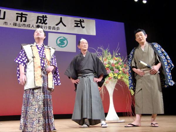 ステージの上で着物を来たちょんまげ姿の男性3名が立っている写真