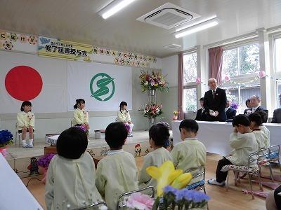 右側にいる市長が話をしており、舞台の上の椅子に座っている卒園生3名と向い合うように椅子に座っている在園生が話を聞いている様子の写真