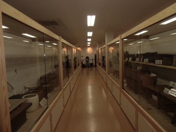 美術館の中のショーケースの中に陶器のようなものが飾られ、その奥に3名の男性が立っている写真