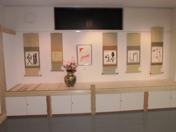 飾られた6つの作品とその前に置かれた花瓶に入った花の写真