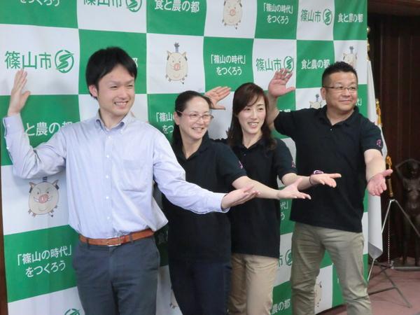 手のひらを上にし左手を前に出し、右手を頭の横に置きポーズをとり記念写真を撮っている丹波篠山楽空間一期一会の男性2人と女性2人の写真