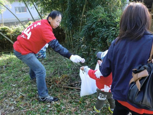男性が拾ったごみを小さい男の子のゴミ袋に入れようとしている様子の写真