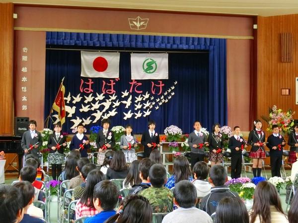 舞台の下に卒業生が横に一列に並んでいるところを在校生が見ている写真