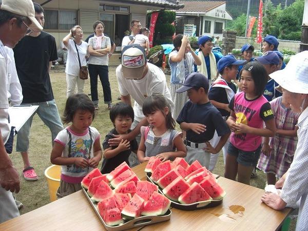 切ったスイカが置かれたテーブルの周りに子どもたち集まっている写真