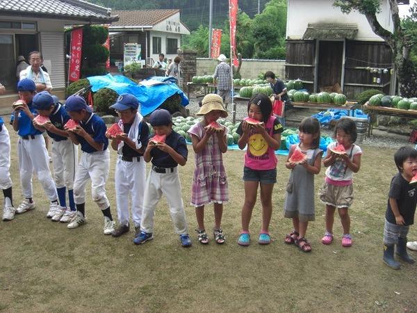 10人ほどの子どもたちが横一列に並んでスイカを食べている写真