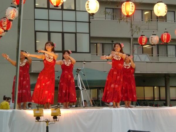 真っ赤なドレスを着て、頭と首に飾りをつけてフラダンスを踊っている写真