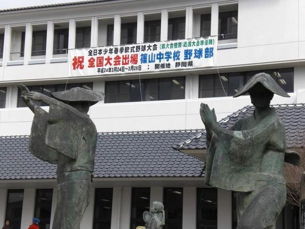 篠山市役所前の銅像があり、その後ろに市役所に掲げられている「祝 全国大会出場 篠山中学校 野球部」と書かれた横断幕の写真