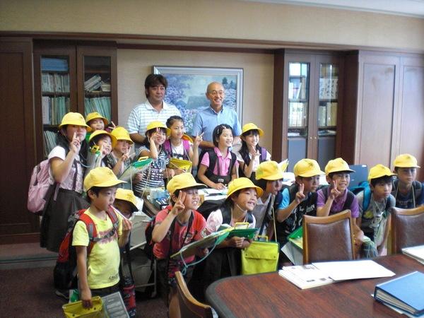 市長の前に集まってピースサインをしている小学生の生徒たちと、男性の写真