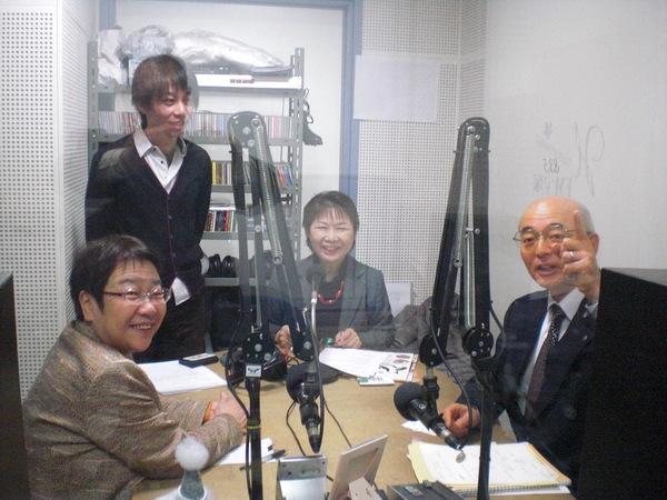 ラジオ局の部屋で局員3人と市長が笑顔で外に向かって話をしている写真