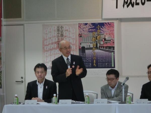 マイクを持った市長が斜め前を向いて話していて、横には二人男性が座っている写真