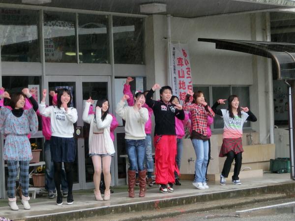 ピンクのジャンパーと私服の大人たちがポーズを決めて楽しそうに踊っている写真