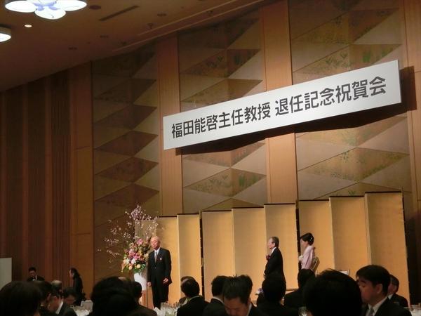 退任記念祝賀会で舞台に市長が立ち少し離れた所に先生と着物を着られた方が写っている写真