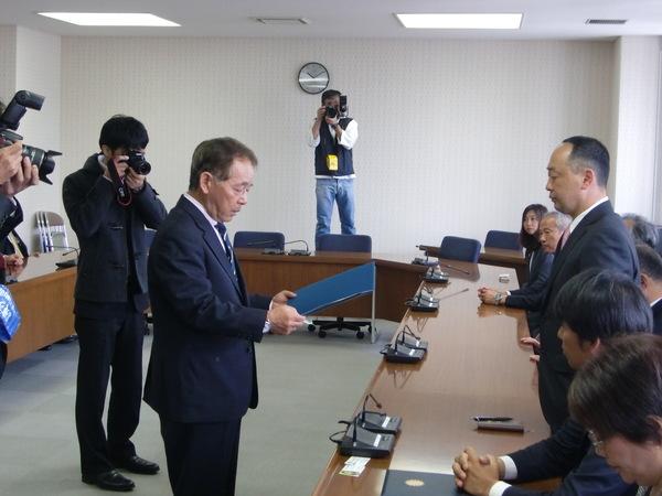 男性が当選者に当選証書を渡しているところを3名のカメラマンが撮影していてる写真