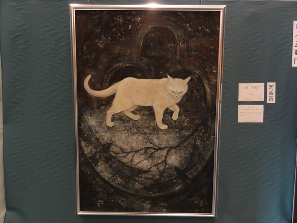 金色の額縁の中、闇のような背景の中央ににうす茶色の猫が描かれている様子の作品