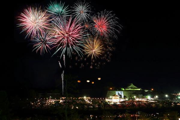 ライトアップされた城の横に打ちあがる色とりどりの花火の写真