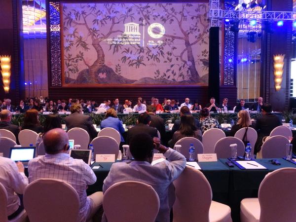 大きなスクリーンと席について会議に参加している各国の代表者の写真