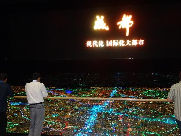 スクリーンに映された、国際化大都市を目指される成都市のライトアップされた街並みの様子を見ている関係者の写真