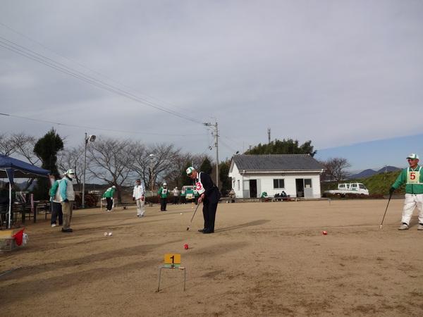 白地に赤文字のゼッケンを首にかけた男性が1番の的に向かって赤いボールを打っている写真