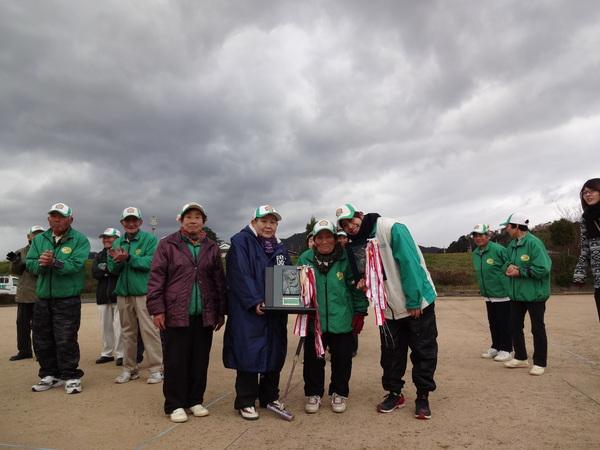 受賞した女性3名と男性1名のグループが盾を手に持っているのを回りの参加者が拍手している写真