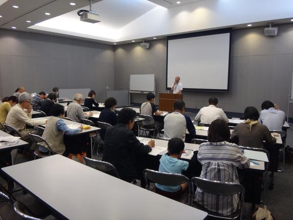 教卓の前でマイクを持った男性が講義をし、参加された方々が真剣に聞いている写真