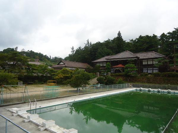 緑色の水がたまるプールと、古風な建物の写真