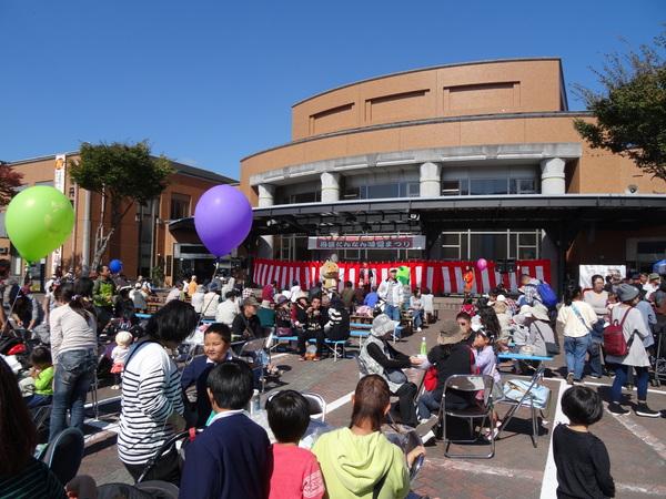 まつりのステージを見ている人々と飲食をしている人々の写真