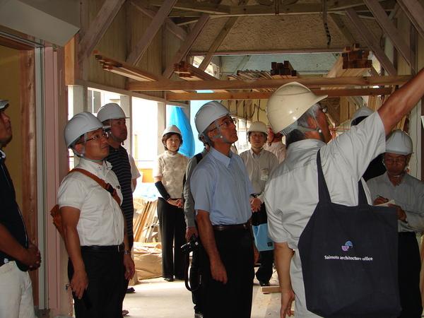 工事中の篠山小学校木造校の校舎内で、関係者の方が上の方に指をさしており、示されている方をヘルメットを被った市長たちが見ている写真