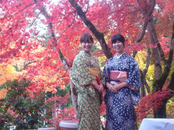グリーンとブルーの着物を着た女性2人が、真っ赤な紅葉の前で記念写真