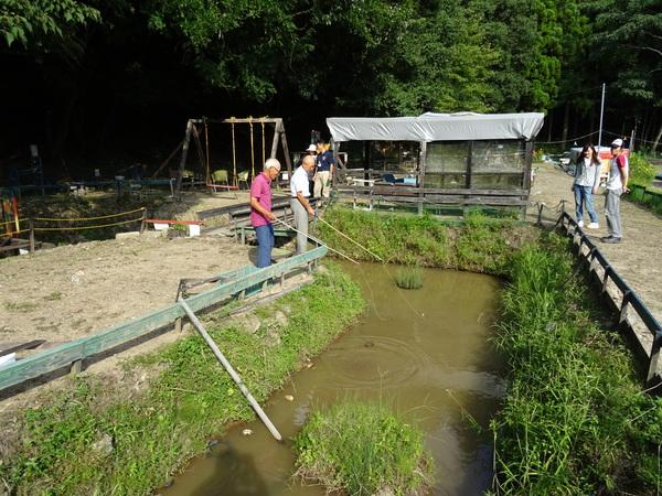 小さな池のような場所で、市長と紫色の洋服の男性が竹に紐を吊るして、魚釣りをしている様子の写真