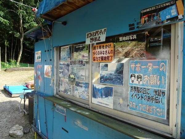 青い小屋のような建物の窓にポスターや写真、募集案内のお知らせ等が貼られている様子の写真