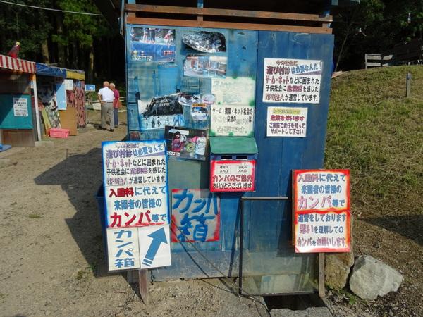 青い小屋のような建物の横の壁に写真、募集案内のお知らせ、カンパの依頼の文章が貼られている様子の写真