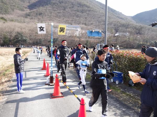 鉢巻きにウインドブレーカー姿の高校生陸上部や野球のユニホームを着た男の子らが走っている写真