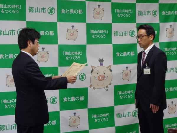 篠山市と書かれた壁の前で男性が表彰を受けている写真