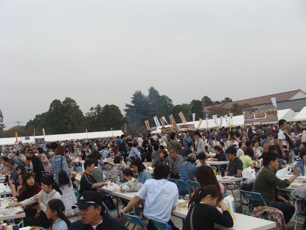 沢山並べられたテーブルで食事をする大勢の参加者の写真