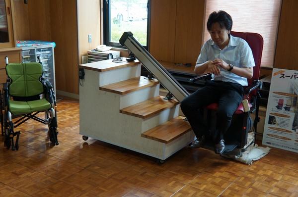 男性が車いすに座って、階段昇降機の説明をしている様子の写真