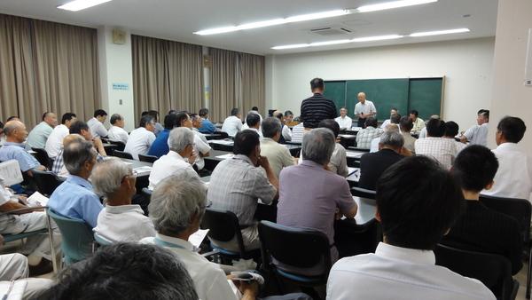 着席する沢山の会議参加者と、立っている男性、その前にマイクをもって立つ市長の写真