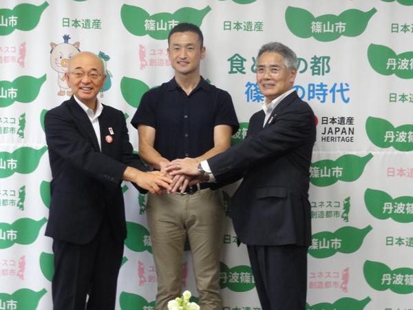 市長と平野 寛さん、スーツを着た男性の3名で、両手を重ねている写真