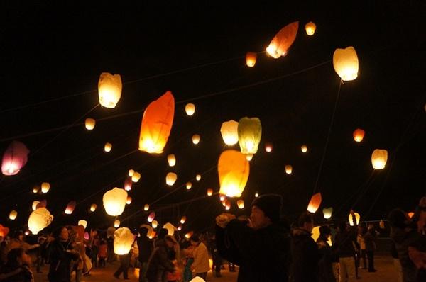 参加者たちがランタンを飛ばし、ランタンが空に舞い上がろうとしている写真
