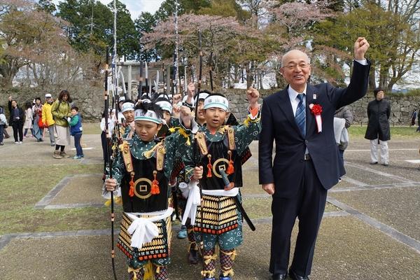 鉢巻きに鎧姿の子供たちが槍を持って市長と一緒に片手ガッツポーズをして記念撮影している写真