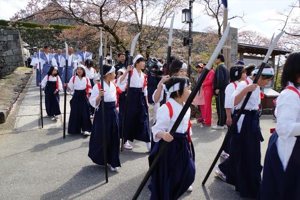 槍を持って鉢巻きに袴姿の女の子らや袴姿の男性らが練り歩いている写真