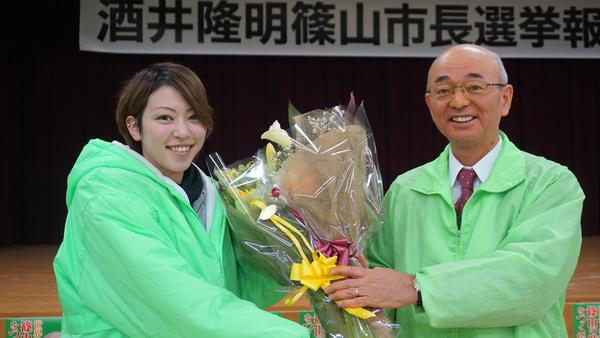 市長が女性より大きな花束を受け取り、2人で花を持ちながら記念撮影している写真