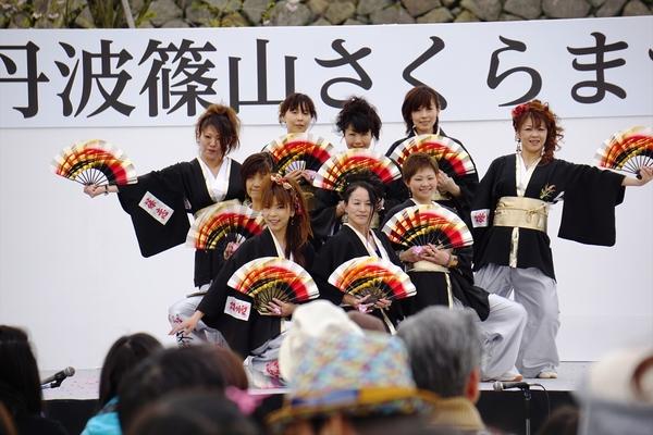 よさこい踊りステージ上で白色のズボンを履いて黒色の羽織を着た女性のチームが扇子を手に最後のポーズを決めている写真