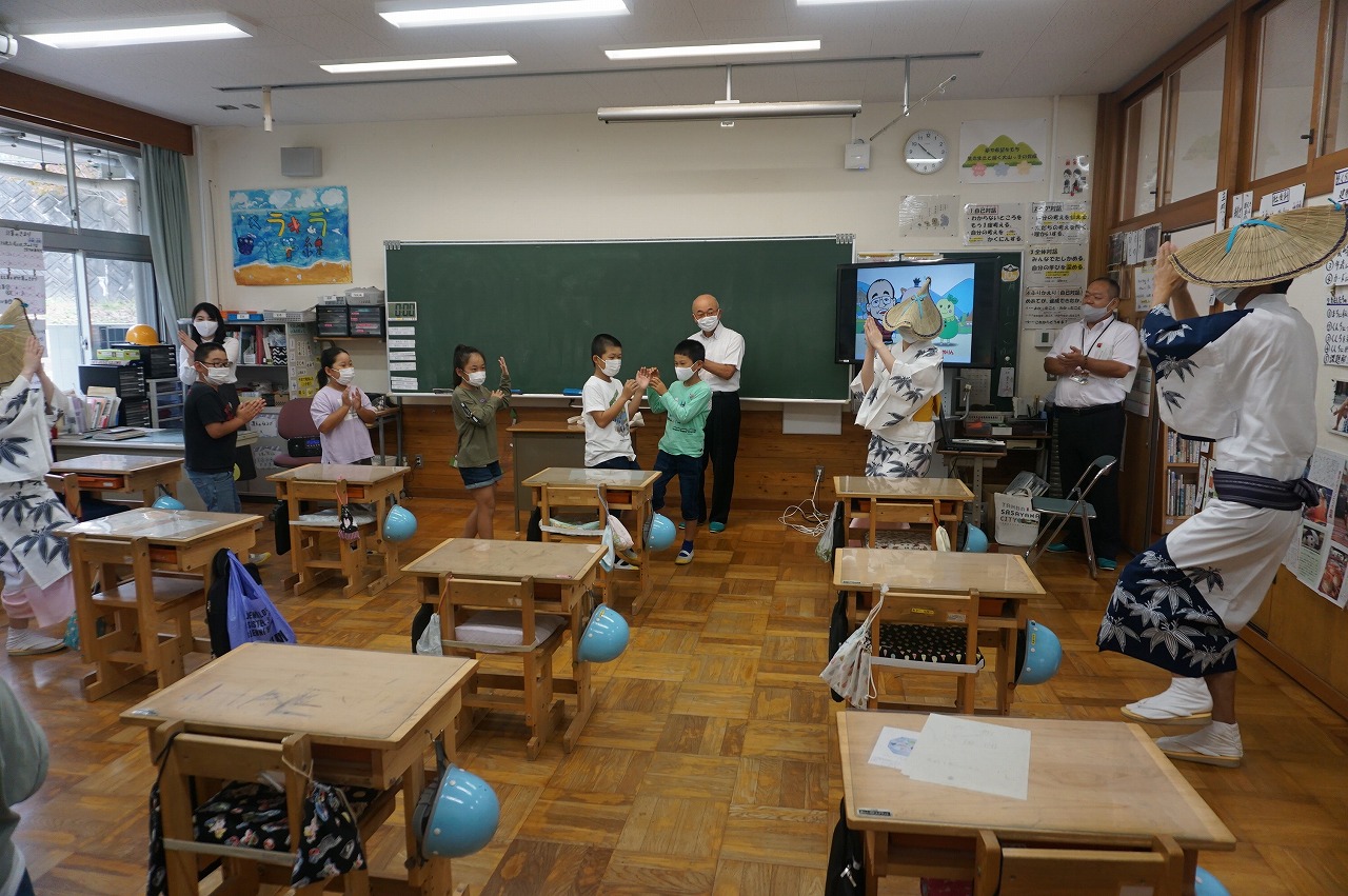 教室で、デカンショ浴衣を着た男性や女性と一緒にこどもたちが輪になってデカンショを踊っている。