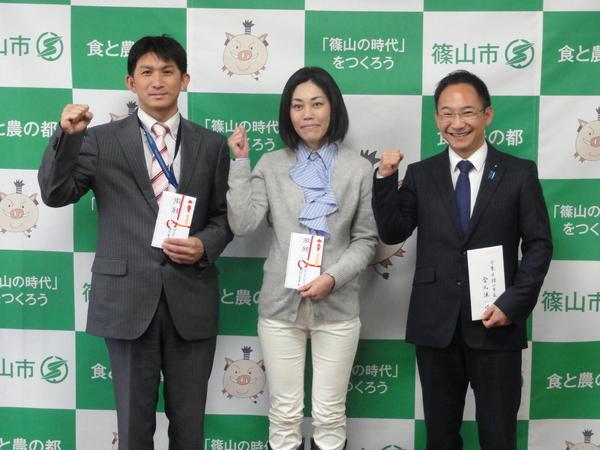 市長より頂いた奨励金及び親書を左手に持ち、右手でガッツポーズをして写っている俣野 秀明さん、梛野 泰子さん、小西 隆紀さんの写真
